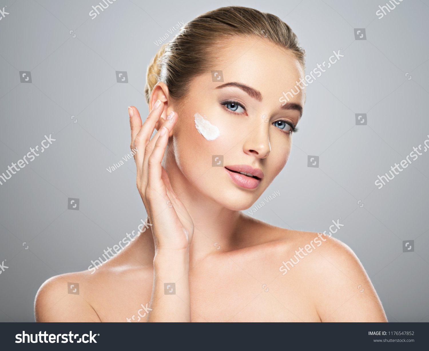 Beautiful young woman gets cream in the face. Skin care concept. Stunning caucasian woman with perfect health clean skin. Portrait of an Attractive girl  with blue eyes, closeup.  #1176547852