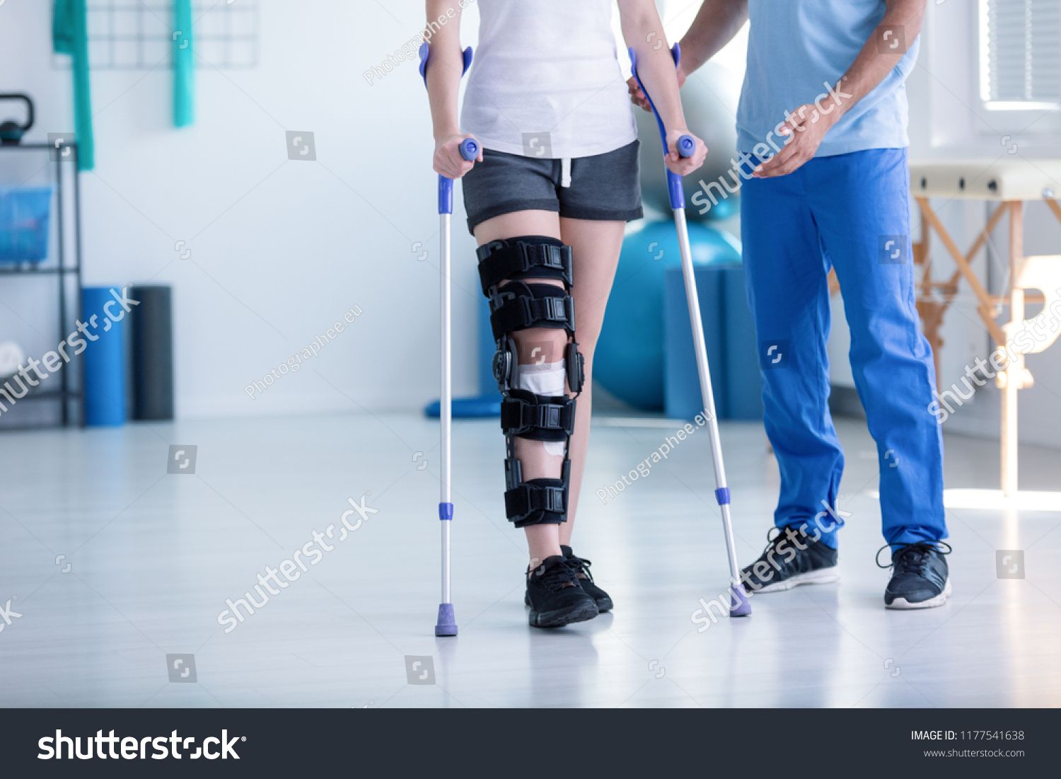 Sport physiotherapist and patient with leg injury during training with crutches #1177541638