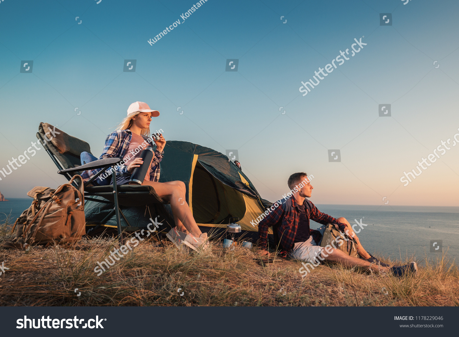 Happy young couple at campsite tent near seaside. Man and woman camp on summer outdoor adventure hiking trip in mountain. #1178229046
