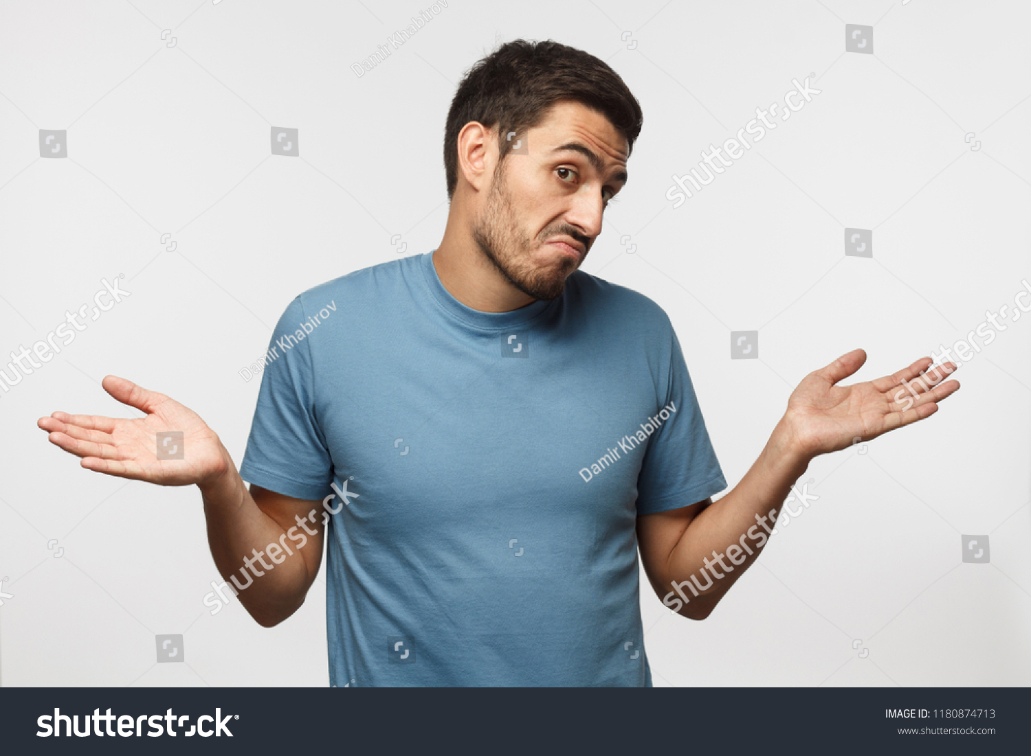 Young man isolated on gray background, showing helpless gesture with arm and hands, mouth curved as if he does not know what to do. I don't know.  #1180874713