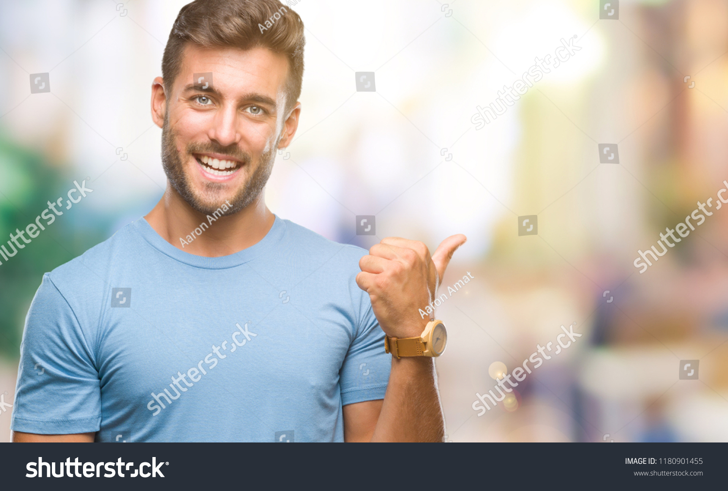 Young handsome man over isolated background smiling with happy face looking and pointing to the side with thumb up. #1180901455
