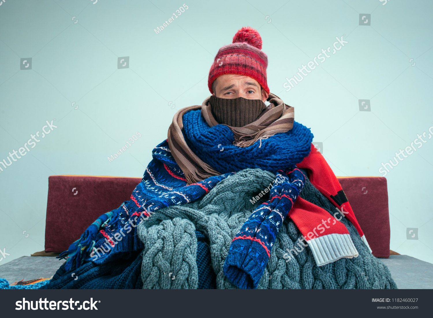 Bearded sick man with flue sitting on sofa at home or studio covered with knitted warm clothes. Illness, influenza, pain concept. Relaxation at Home. Healthcare Concepts. #1182460027