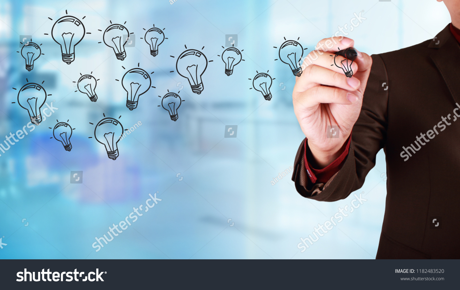 Business concept. Businessman draw on virtual screen with idea light bulb icons flying over. Against blur blueish background #1182483520