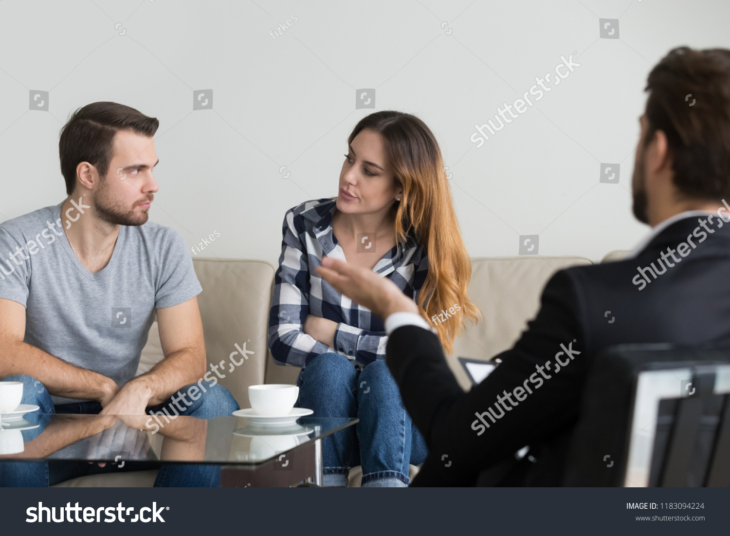Angry divorcing couple sit on couch looking at each other with hate and annoyance, taking family therapy session at psychologist, husband and wife saving marriage seek help from relationships expert #1183094224