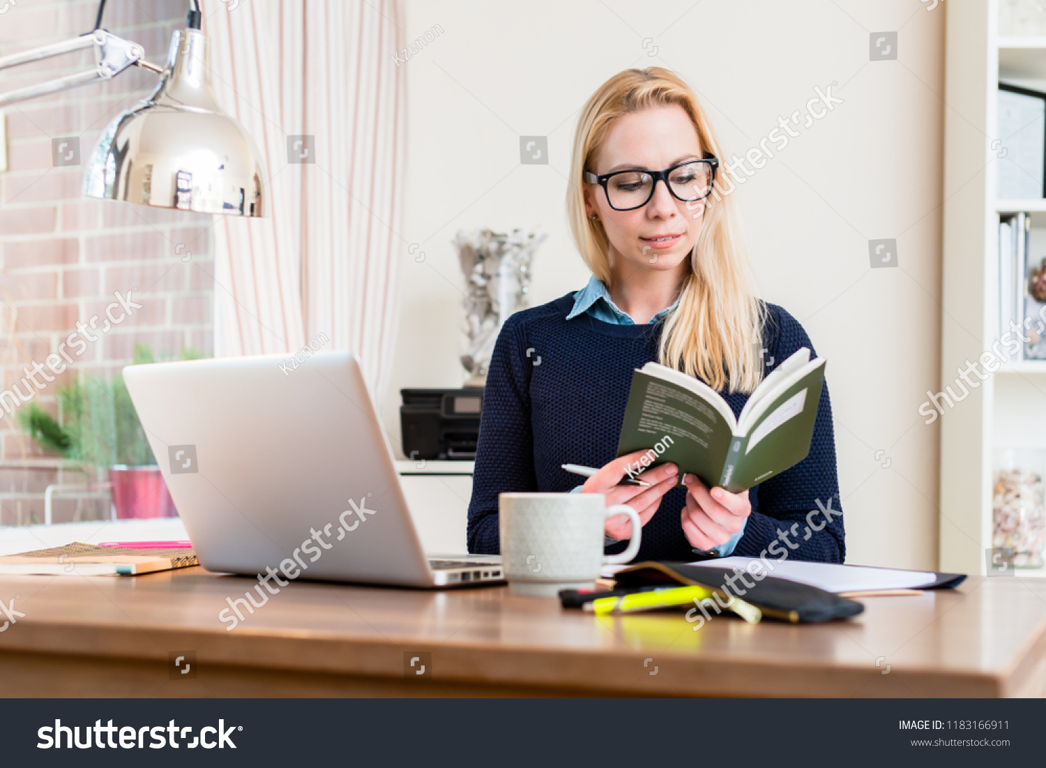 Woman sitting at her desk in office reading book #1183166911