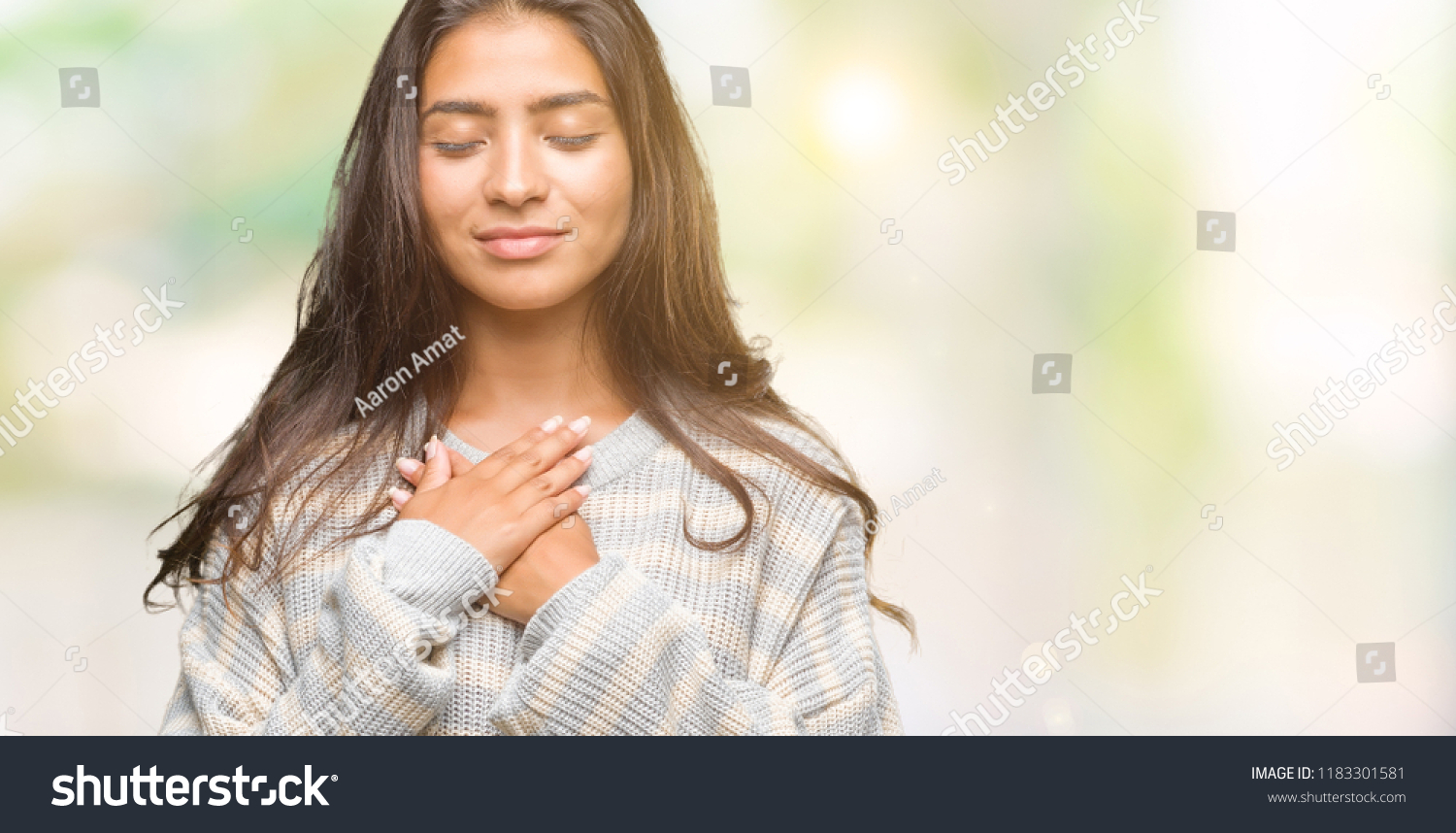 Young beautiful arab woman wearing winter sweater over isolated background smiling with hands on chest with closed eyes and grateful gesture on face. Health concept. #1183301581