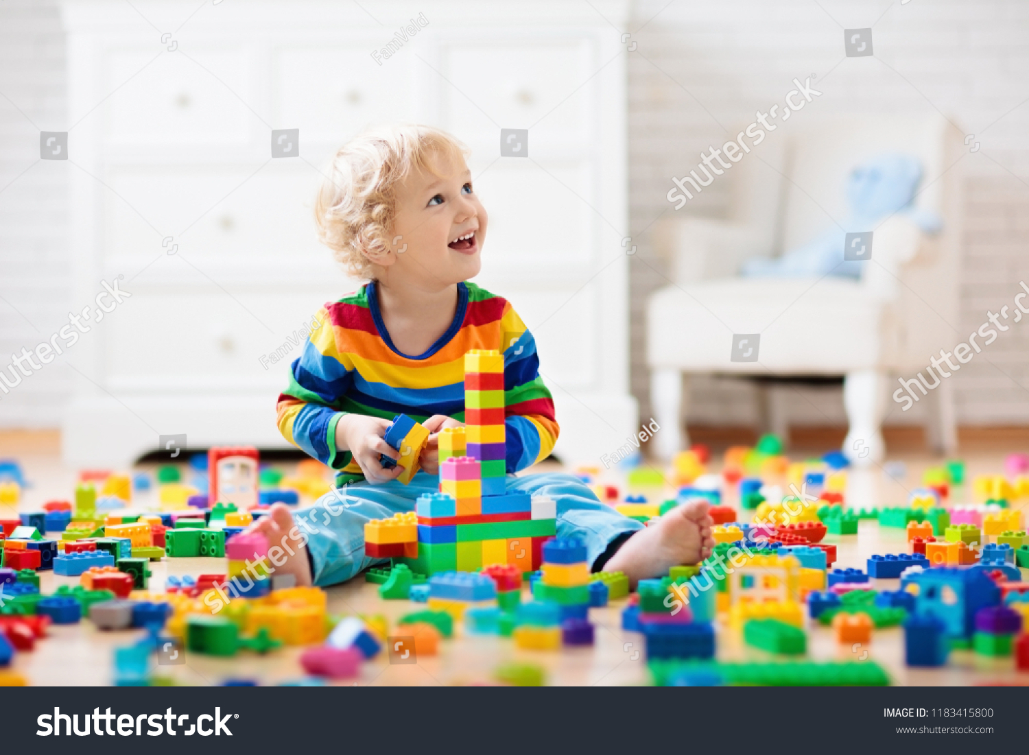 Child playing with colorful toy blocks. Little boy building tower at home or day care. Educational toys for young children. Construction block for baby or toddler kid. Mess in kindergarten play room. #1183415800