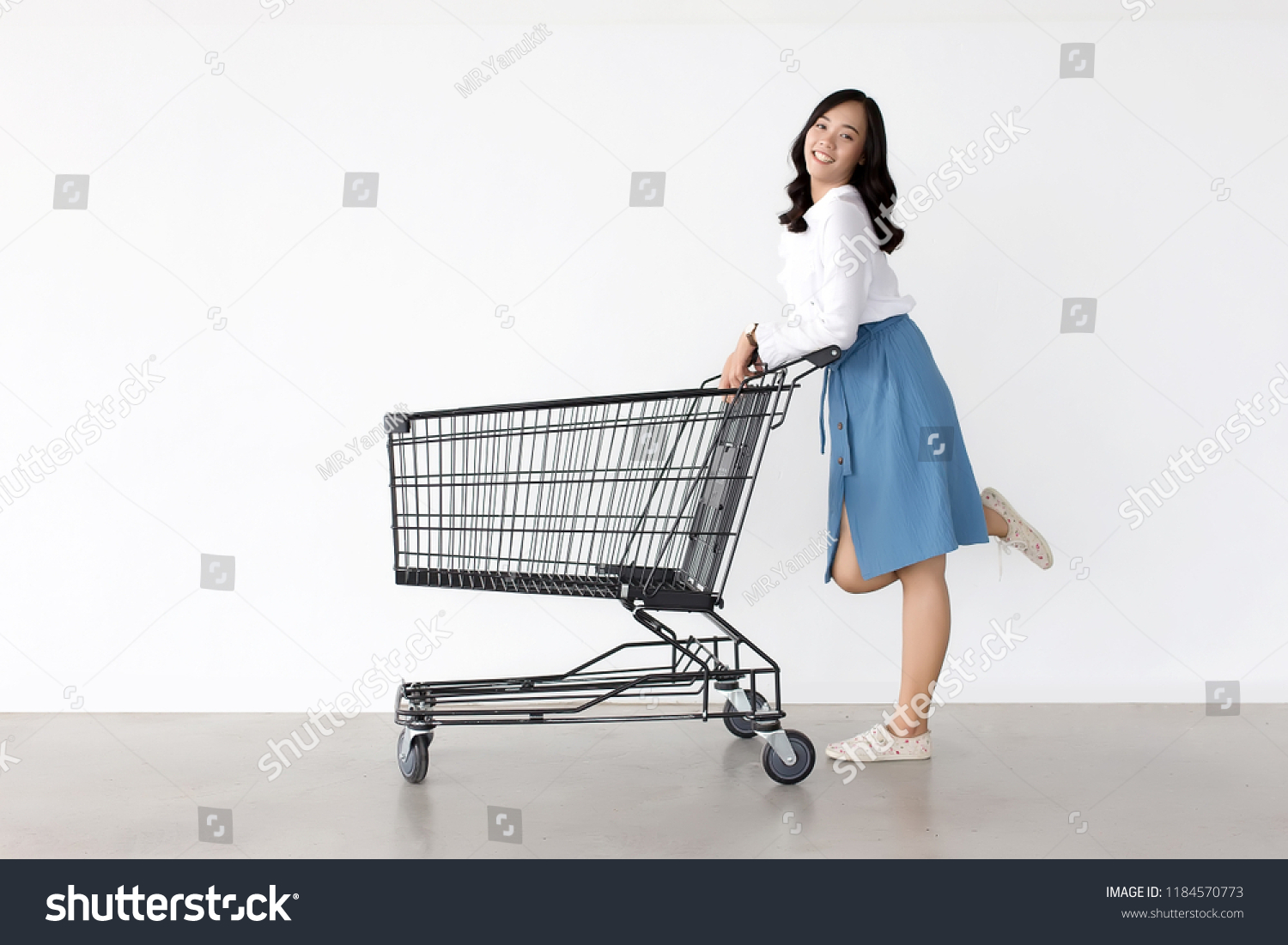 happy asian lady in shopping action with shopping cart on white background.   #1184570773