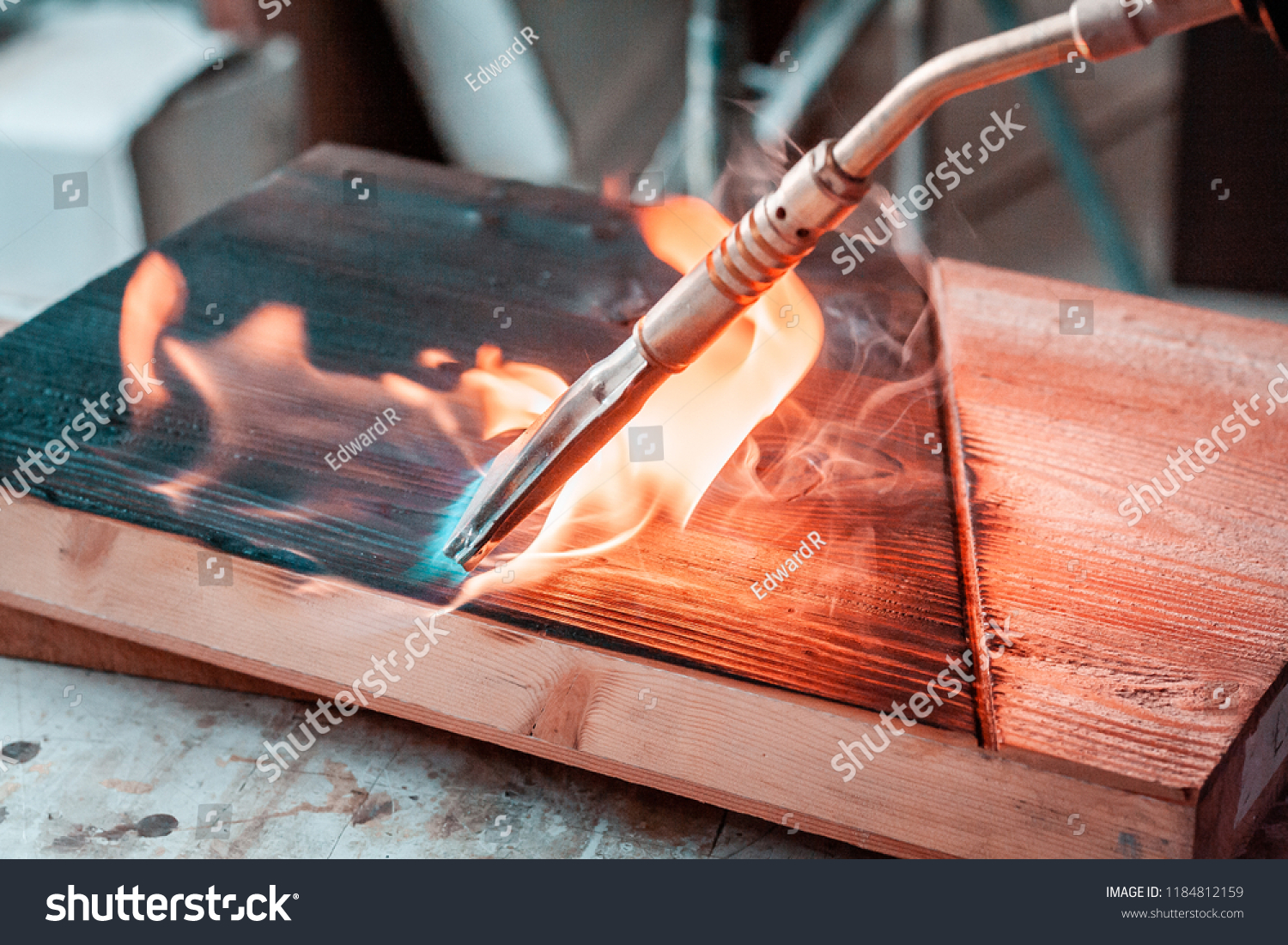 High quality wood planks and slabs, while being burnt with a brass, gas burner in woodshop in Italy. Details of the fire burst, and black wooden texture after the process.  #1184812159