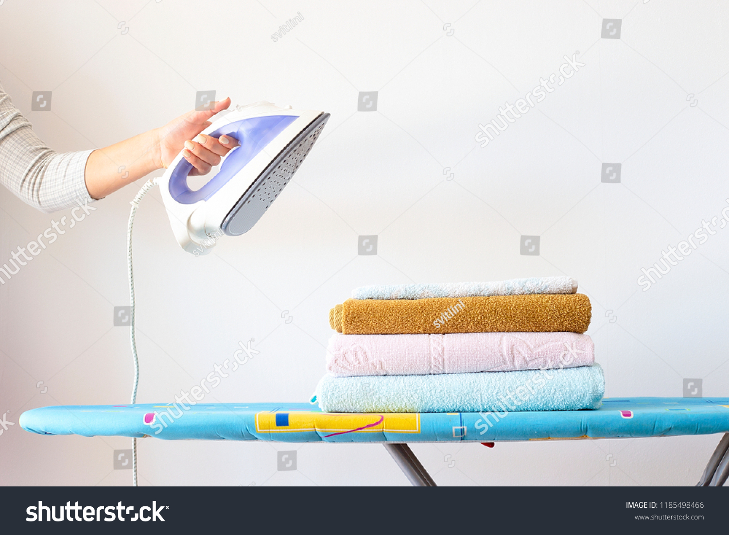 A woman's hand holds an iron over a pile of clean ironed towels on the ironing board. Homework Concept #1185498466