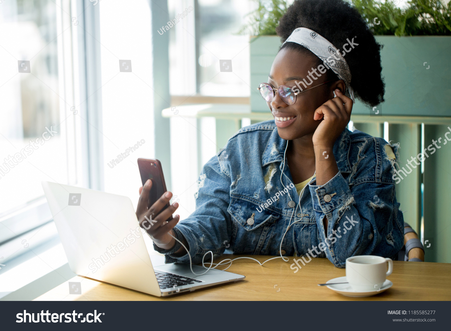 Young african customer client female in spectacles and jeans outfit beaming with joy, spending free time shopping online while sitting in cafe. #1185585277