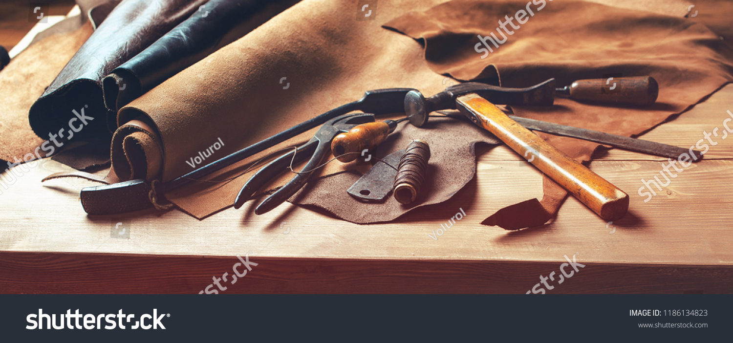 Shoemaker's work desk. Tools and leather at cobbler workplace. Set of leather craft tools on wooden background. Shoes maker tools on wooden table #1186134823