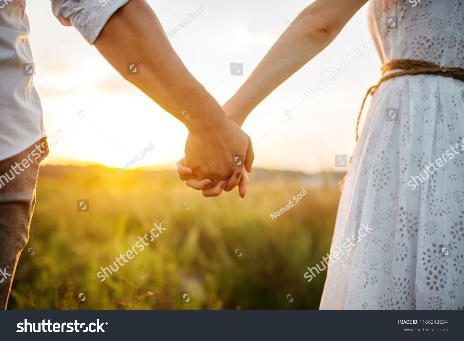 Couple hold hands in green field on sunset #1186242634
