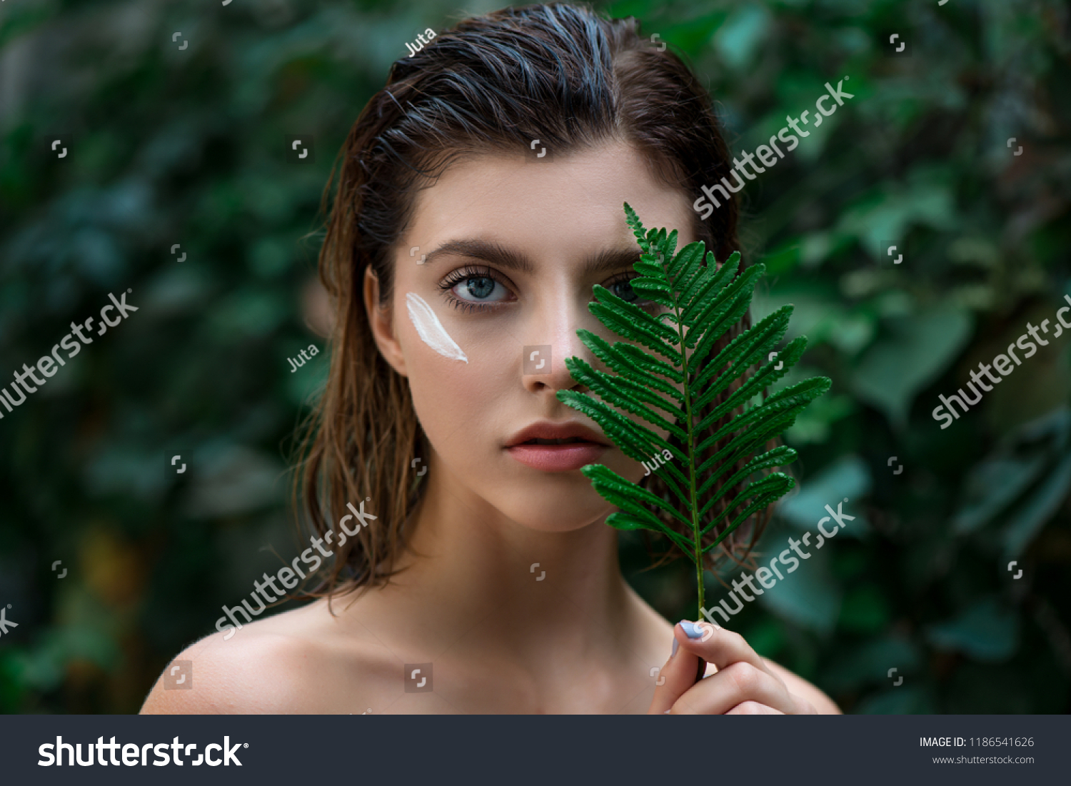 Beautiful young woman with perfect skin and natural make up posing front of plant tropical green leaves background with fern. Teen model with wet hair care of her face and body. SPA, wellness #1186541626