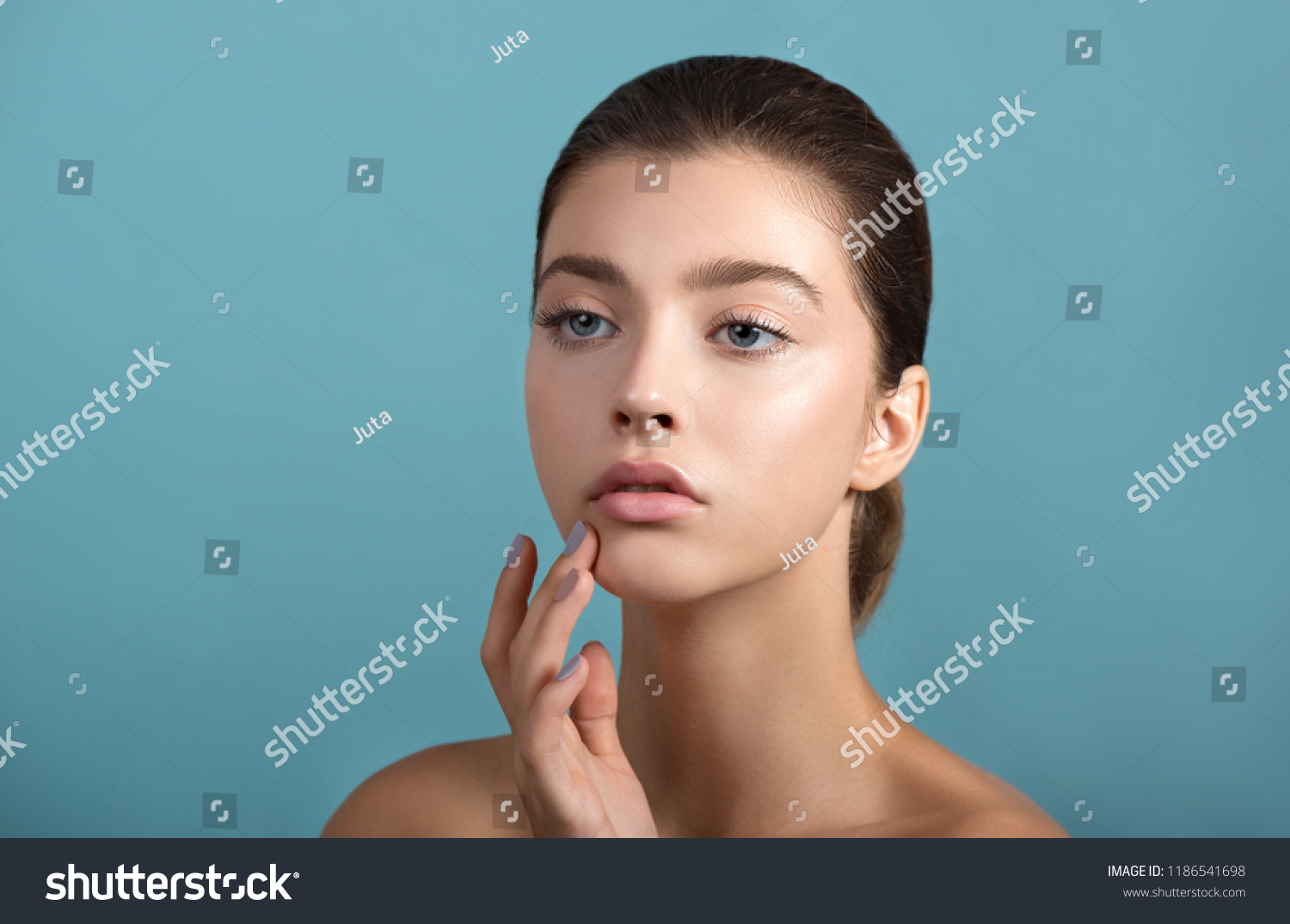 Beautiful young  woman with fresh clean perfect skin. Portrait of beauty model with natural make up and and hand with manicure touching face. Spa, skincare and wellness. #1186541698