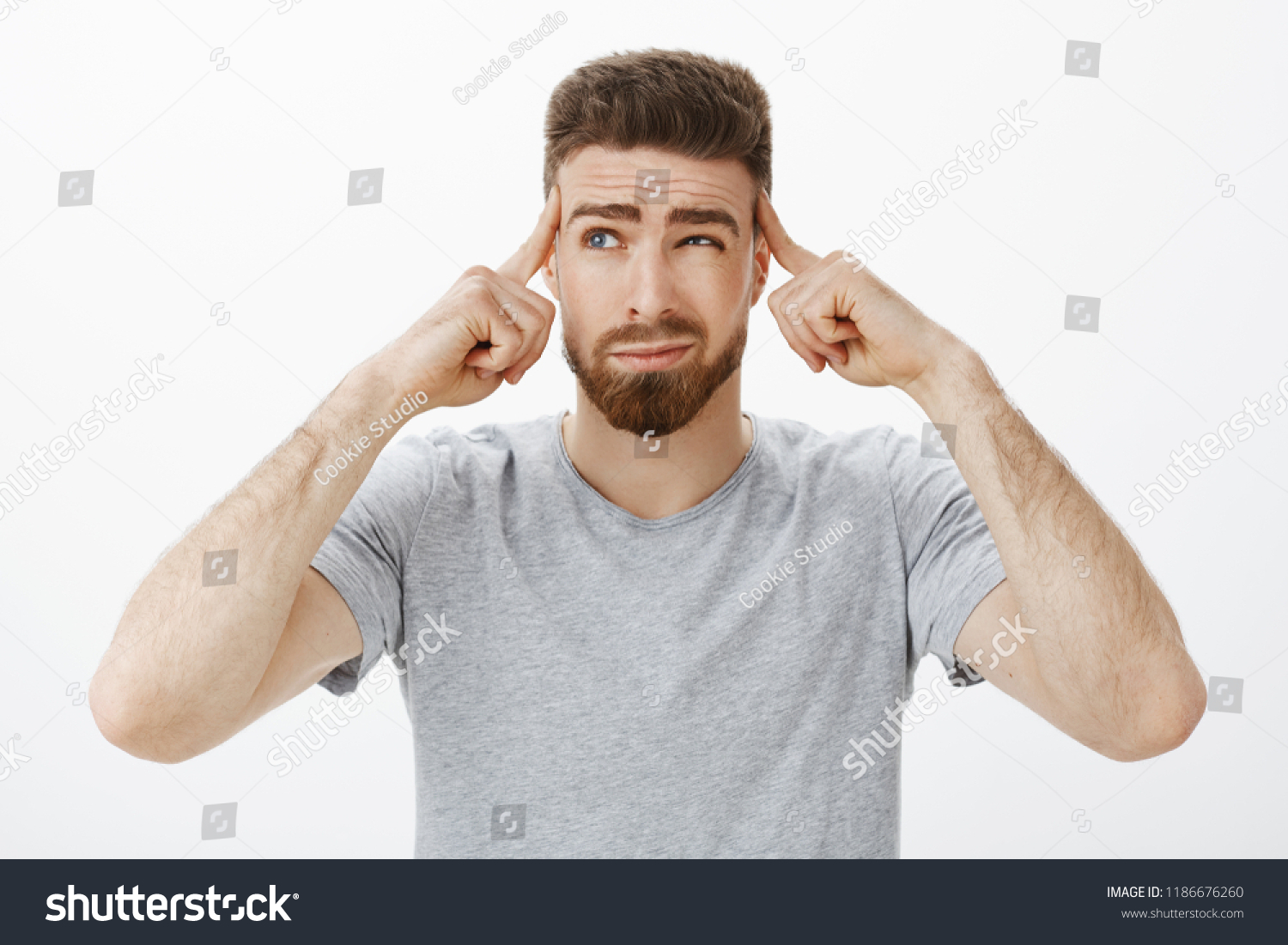 Guy trying focus, think up new plan. Determined, thoughtful handsome charismatic man with beard and blue eyes squinting, smirking holding fingers on temples focusing on importrant game, concentrating #1186676260