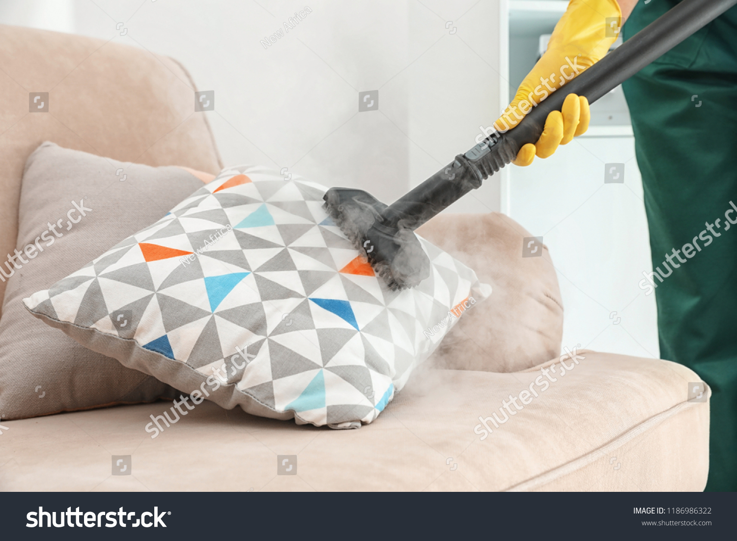 Janitor removing dirt from sofa cushion with steam cleaner, closeup #1186986322