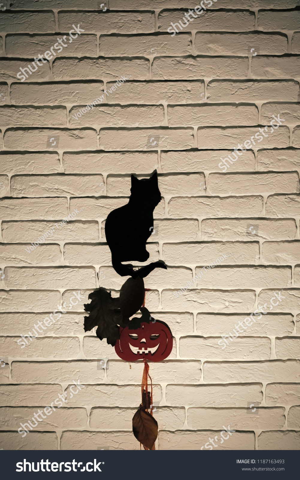 Halloween celebration concept. Black cat and orange pumpkin with tree leaves silhouettes paper cutouts on grey brick wall. Animal totem and holiday symbols. Mystery and superstition #1187163493