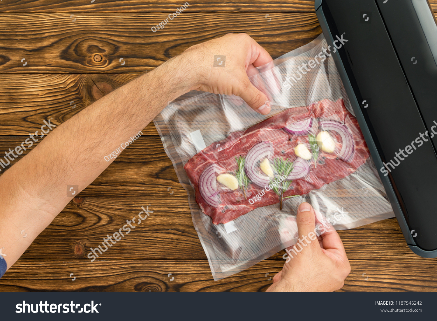 Unidentified adult man sliding plastic packaged meat with onion and garlic into black machine to preserve meat #1187546242