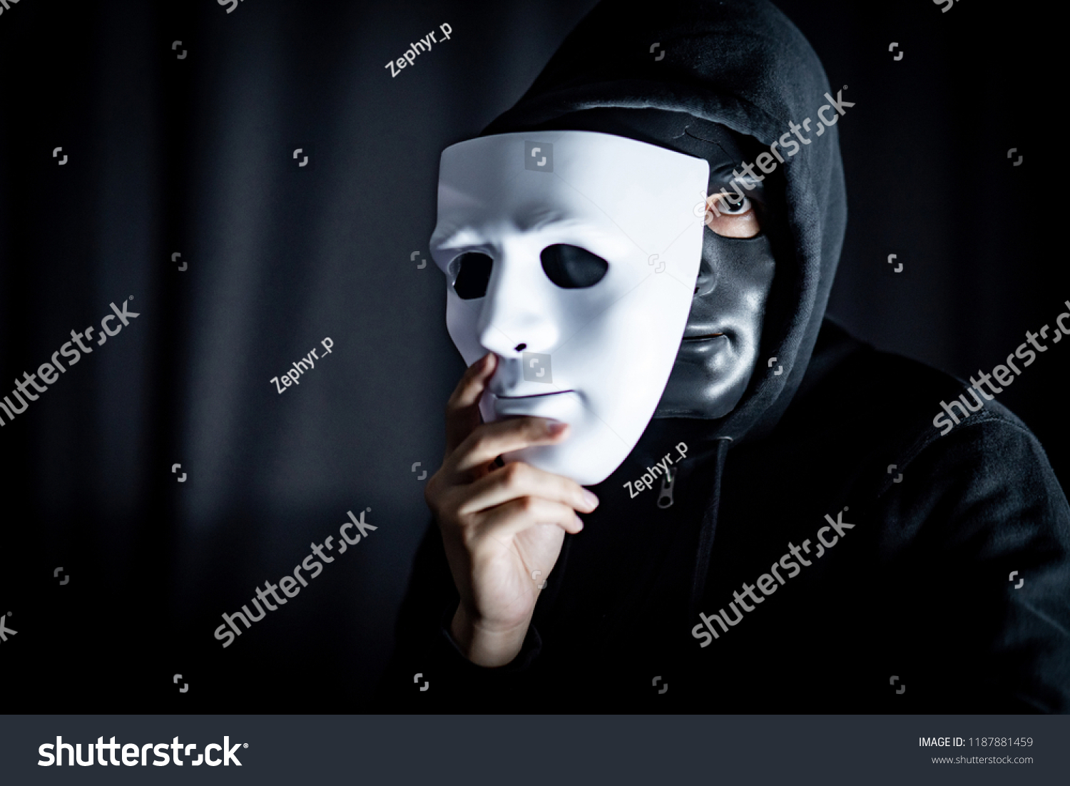 Mystery hoody man wearing black mask holding white mask. Anonymous social masking. Major depressive disorder or bipolar disorder. Halloween concept #1187881459