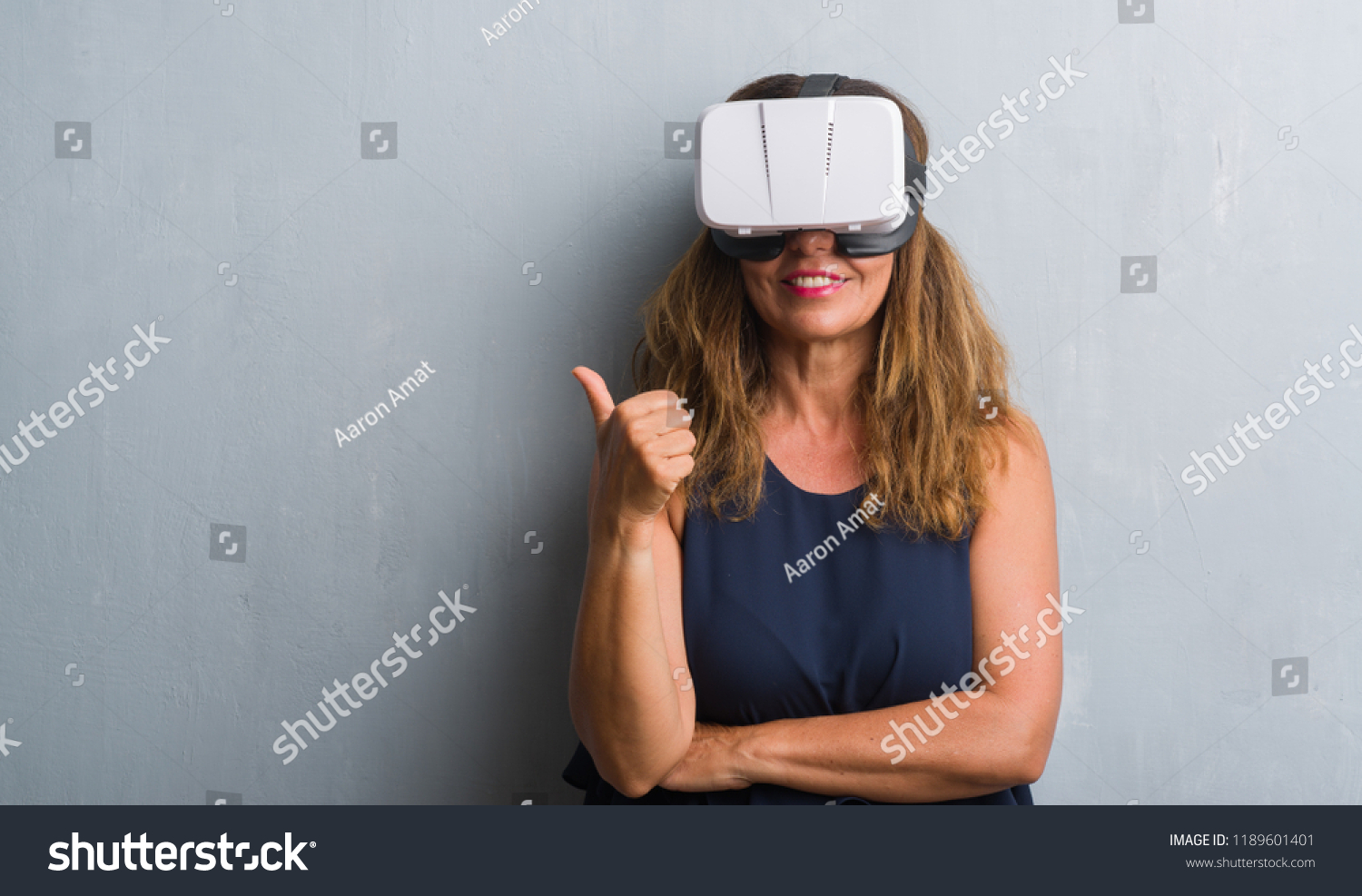 Middle age hispanic woman standing over grey grunge wall wearing virtual reality glasses happy with big smile doing ok sign  #1189601401