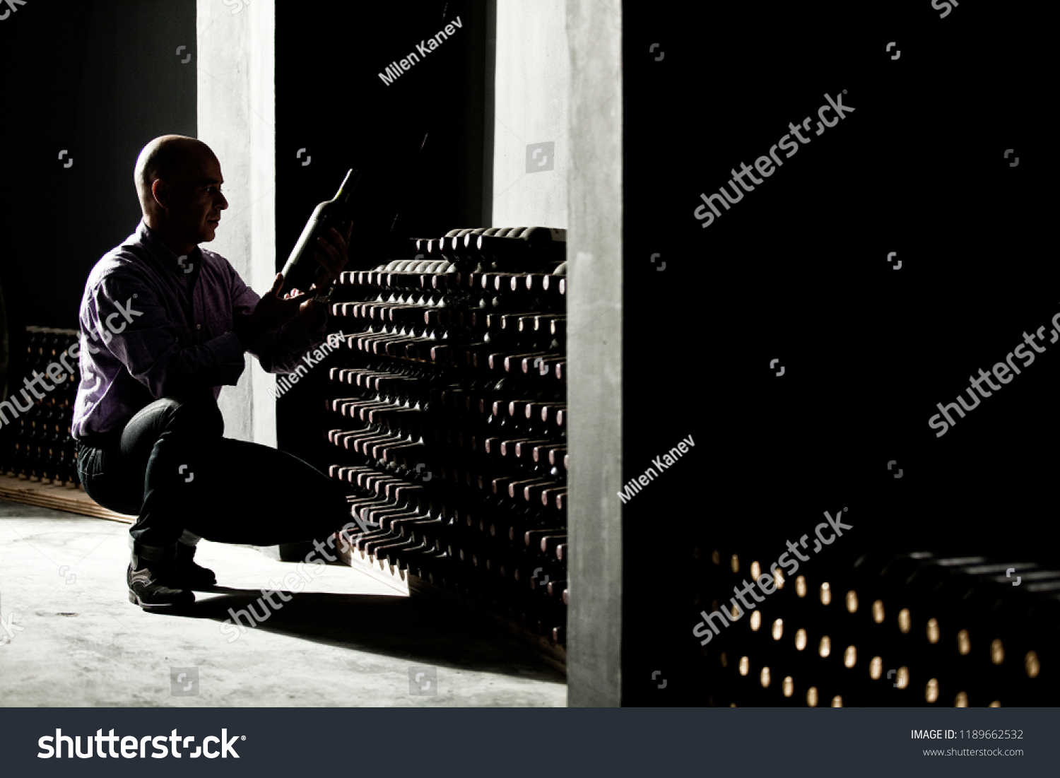 Wine maker checking horizontal bottles in a dark cellar #1189662532