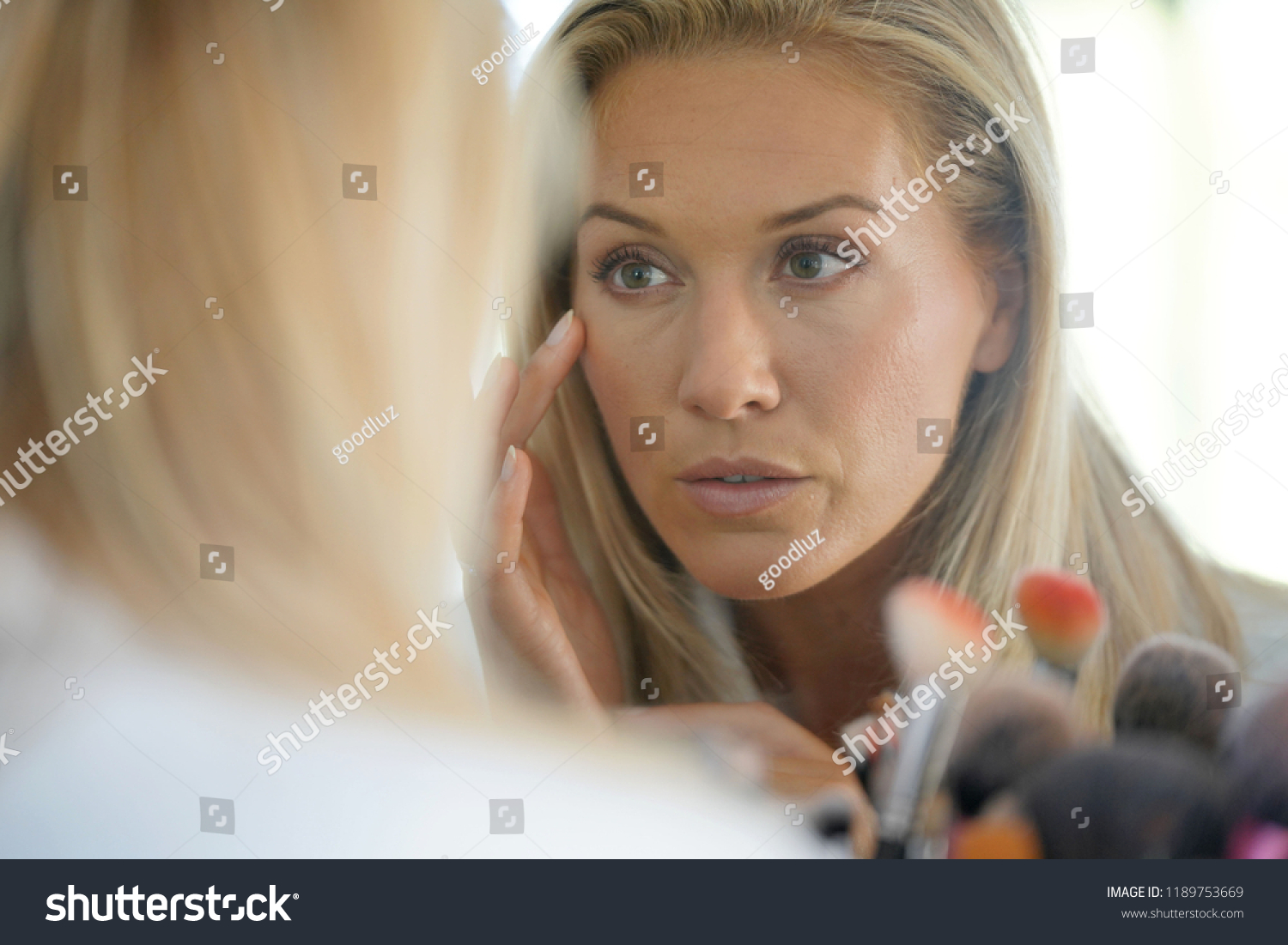 Middle-aged woman looking at her skin in front of mirror #1189753669