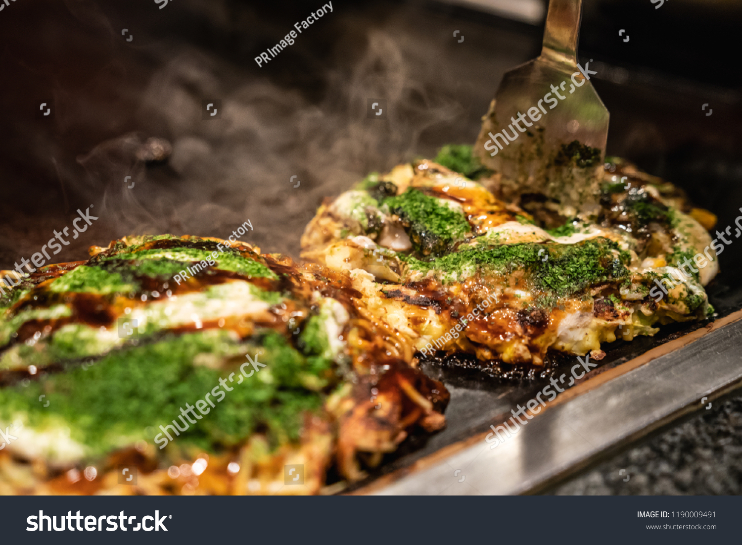 chef use spatula to cut the done okonomiyaki in half on the iron plate, and ready to give the delicious japanese traditional food to the customers #1190009491