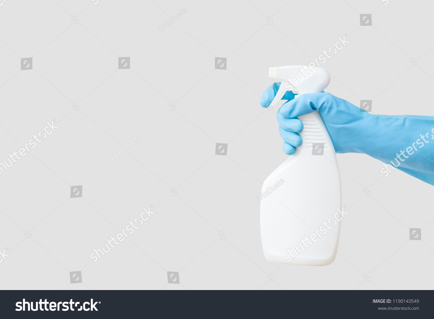 Cleaner's hand in blue rubber protective glove holding a white chemical spray bottle. Empty place for text or logo on gray background. Early spring or regular cleanup. Commercial cleaning company. #1190143549
