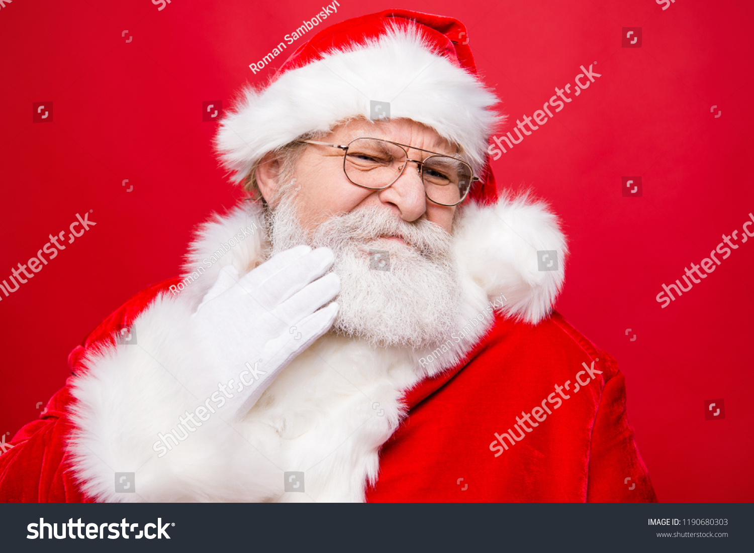 Aged mature stylish confused moody frustration grandfather Santa in costume glasses touch hand gloves to cheek make isolated on red background #1190680303