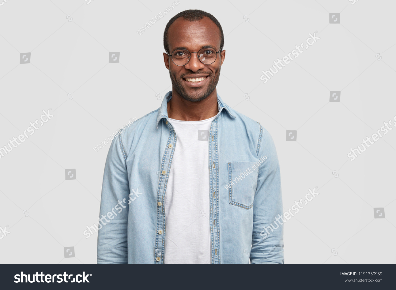 Waist up shot of handsome self confident cheerful male entrepreneur has broad smile, wears round transparent glasses, happy to meet with colleague, dressed in fashionable denim shirt isolated on white #1191350959
