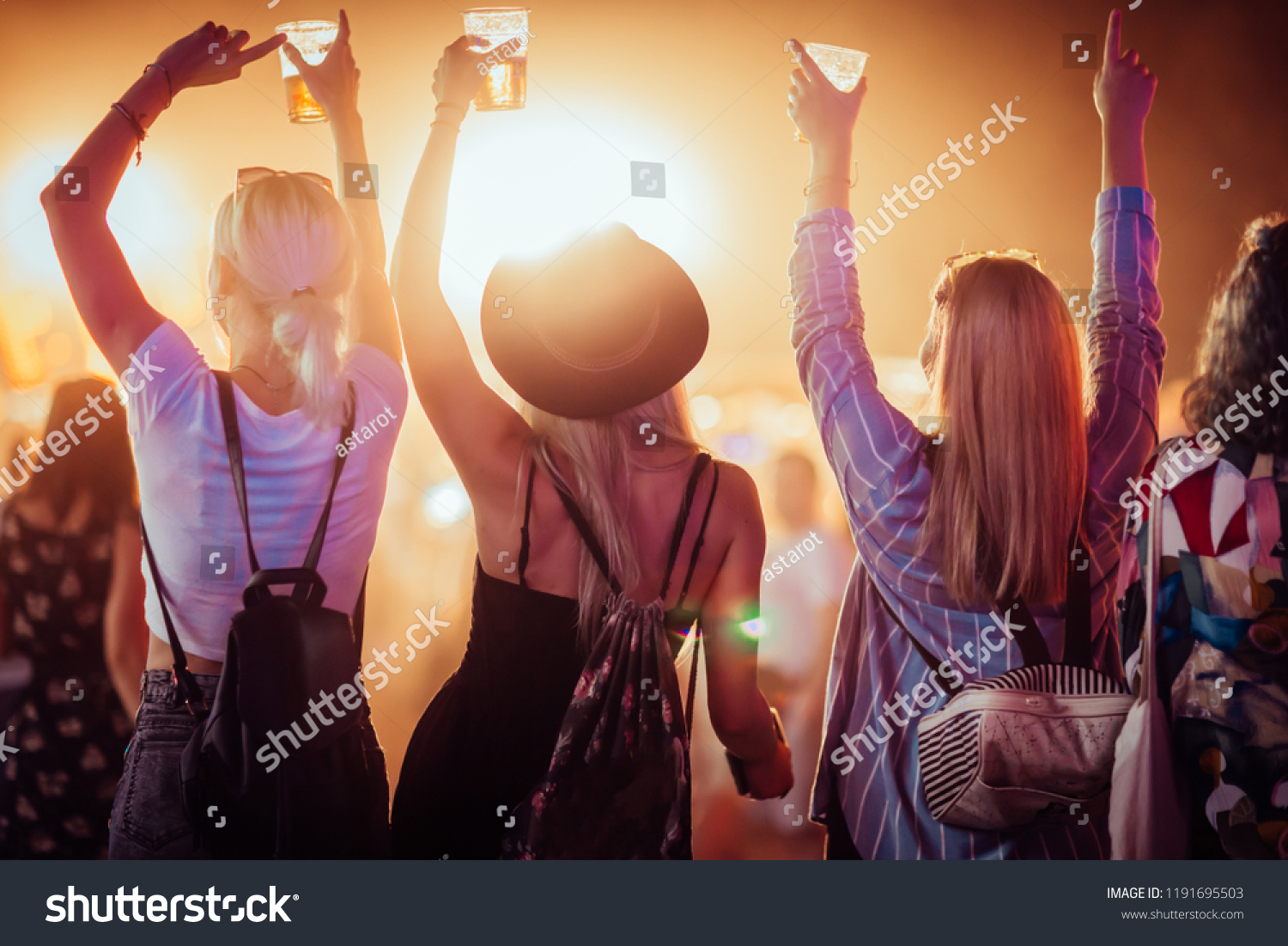 Back view of group of female friends at music festival drinking beer and dancing #1191695503