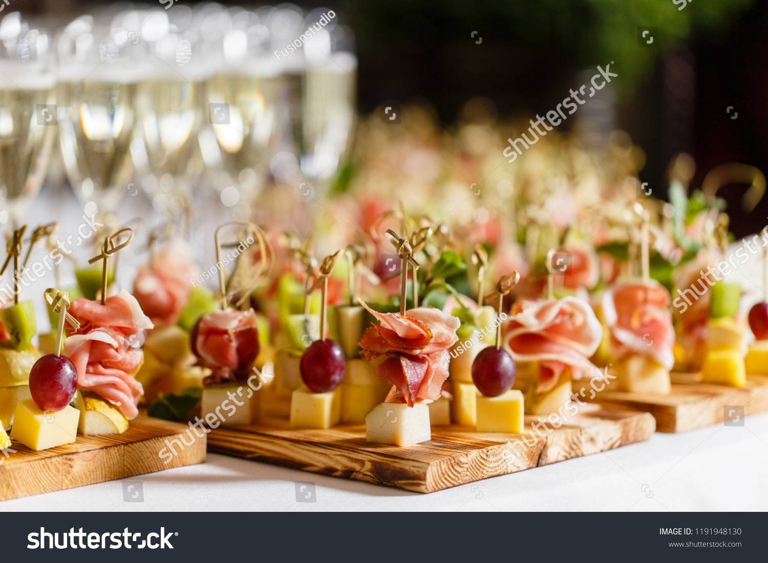 the buffet at the reception. Glasses of wine and champagne. Assortment of canapes on wooden board. Banquet service. catering food, snacks with cheese, jamon, prosciutto and fruit #1191948130