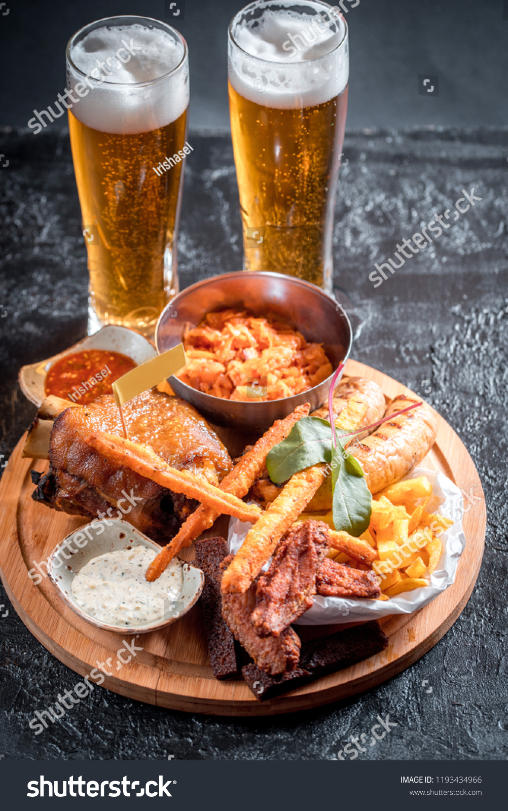 Foamy beer in a glass, hot appetizer, chicken wings, sauce in a beautiful served bowl. Catrofel and other deep-fried vegetables. unhealthy food. unhealthy food. many calories #1193434966