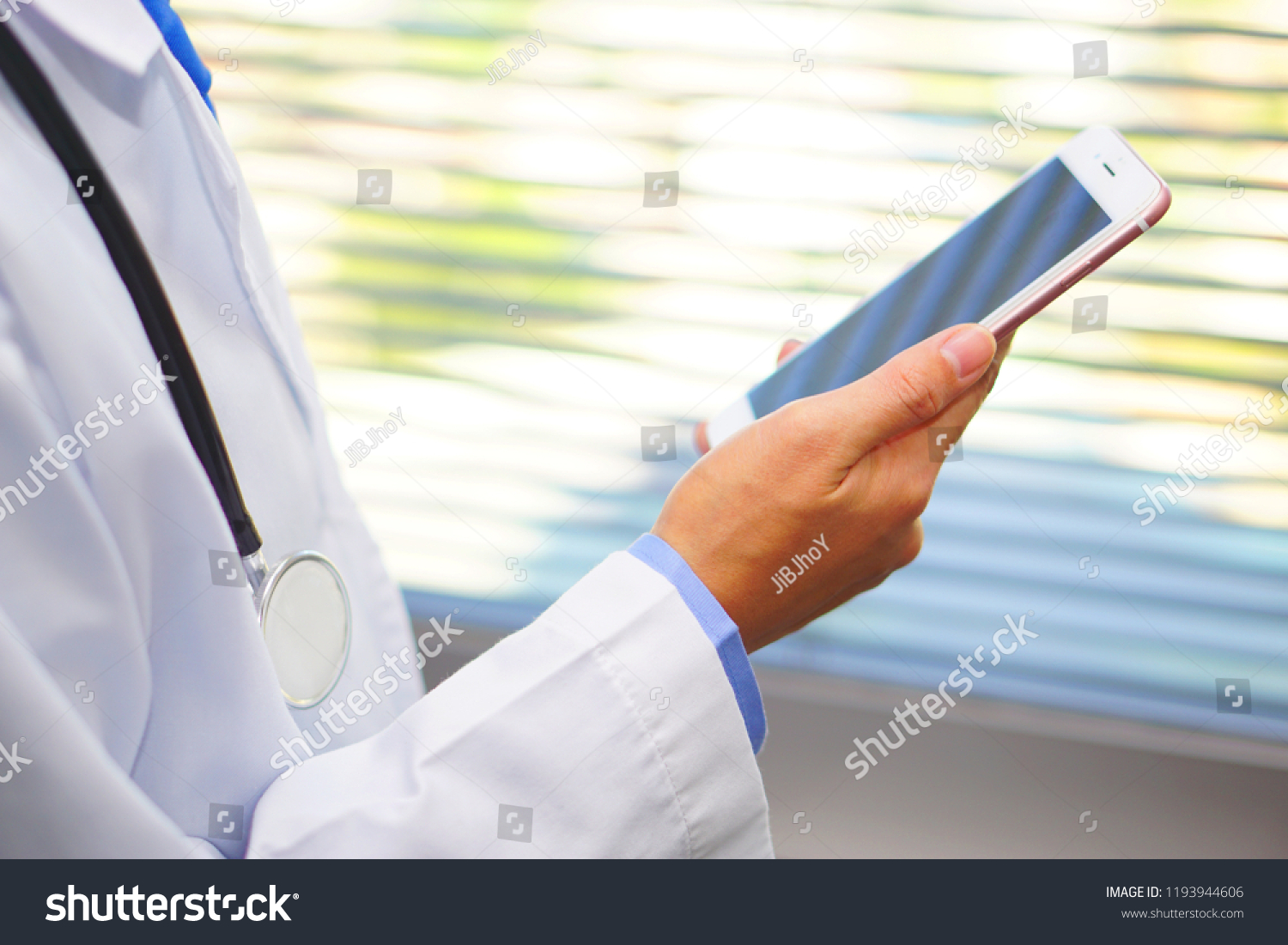 Male doctor in white coat is using a modern smart phone device with touch screen in hospital. Healthcare and medical concept. #1193944606