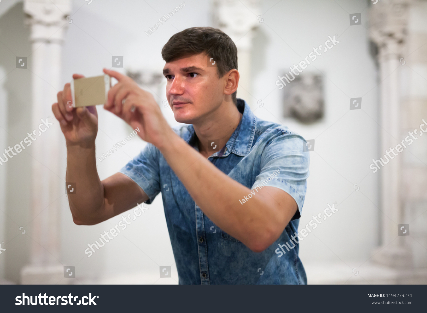 Man looking at exposition of antiquities and taking pictures on his phone in historical museum #1194279274