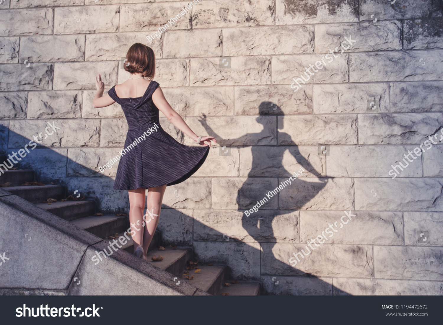 Young beautiful brunette girl in blue dress dancing with her shadow on stone wall background, concept of inspiration, enthusiasm and aspiration #1194472672