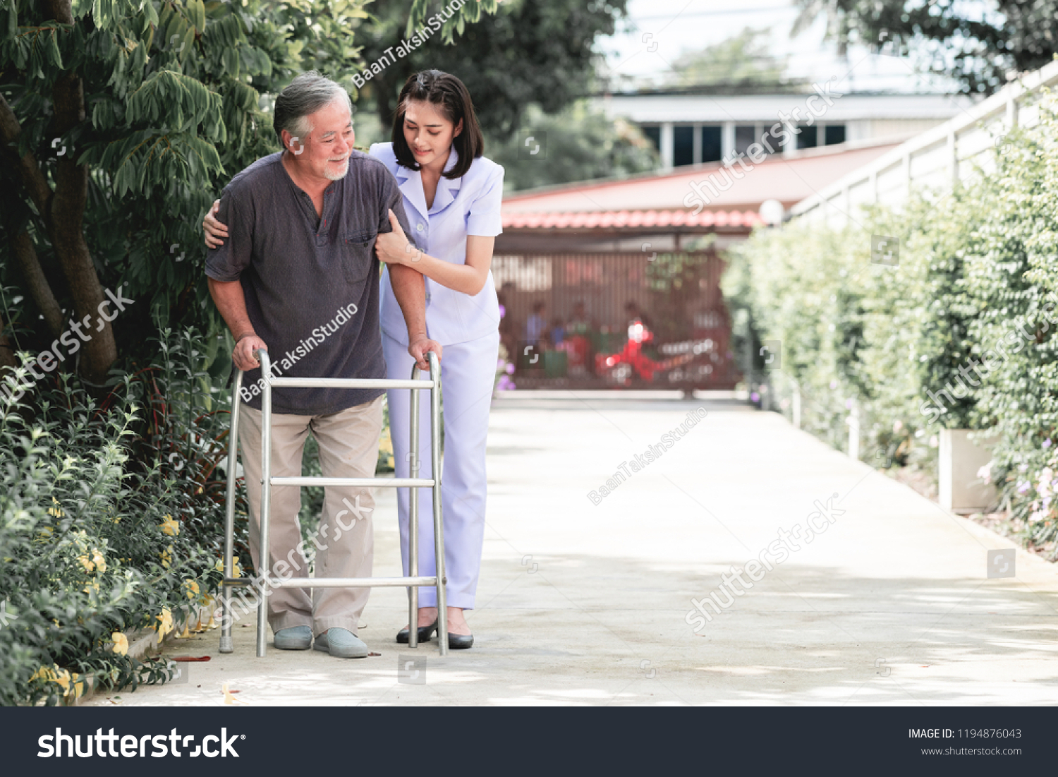 Nurse with patient using walker in retirement home. Young female nurse holding old man's shoulder in outdoor garden walking. Senior care, care taker and senior retirement home service concept. #1194876043