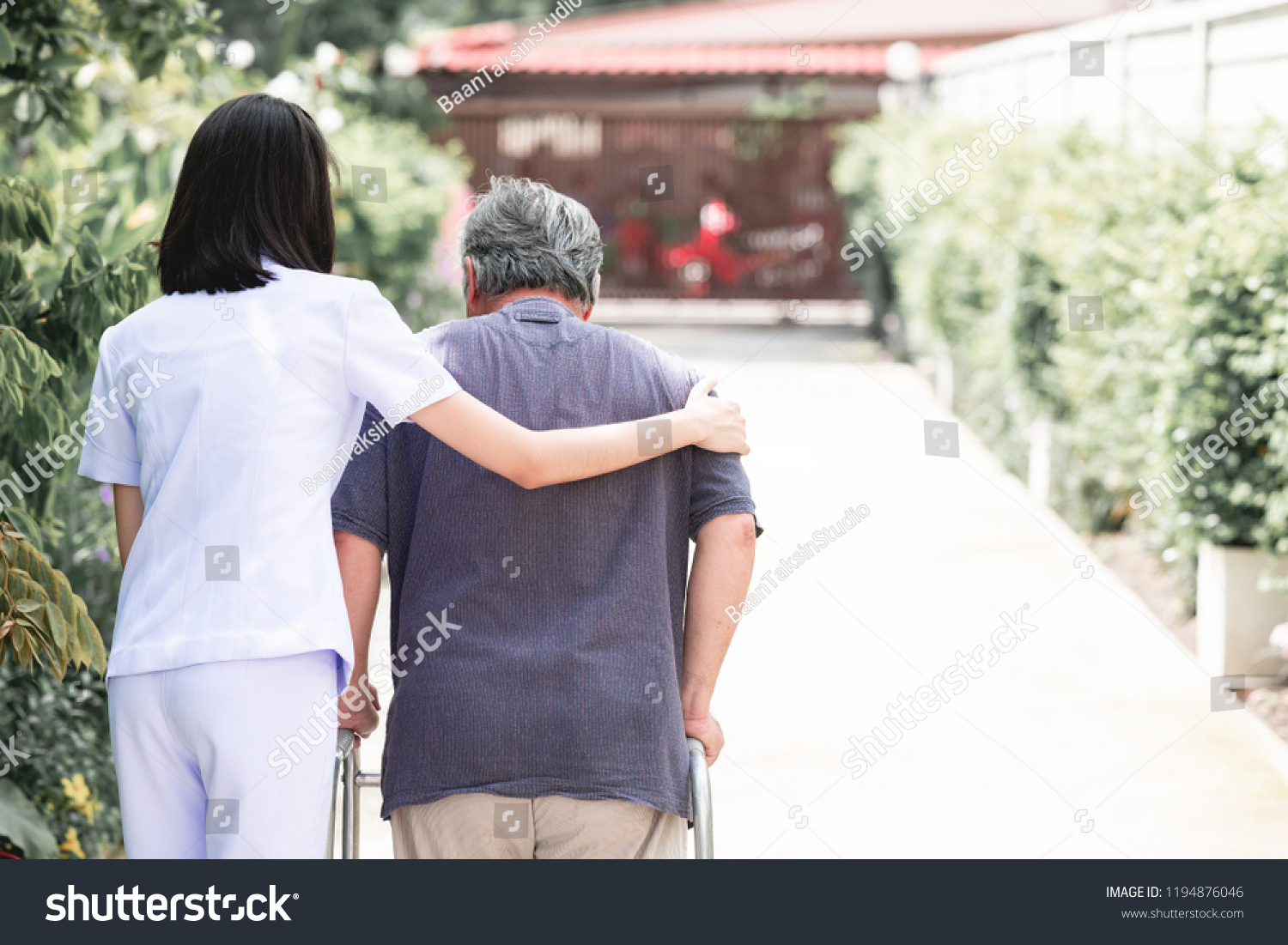 Nurse with patient using walker in retirement home. Young female nurse holding old man's shoulder in outdoor garden walking. Senior care, care taker and senior retirement home service concept. #1194876046