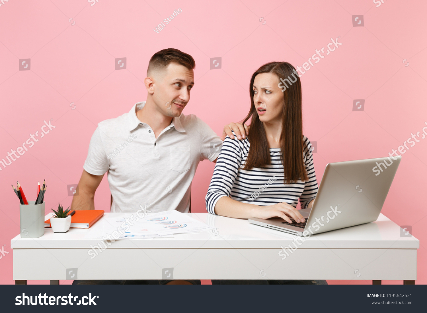 Two young business woman man colleagues sit at white desk isolated on pastel pink background. Sexual harassment, assault lustful boss, intimidation, work ethic, stress, design concept. Co working #1195642621