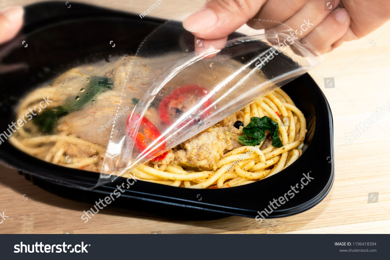 Food Delivery service: Woman hands holding open cling wrap and take out food in plastic boxes on wood background. concept online order take away food ready for home delivery. #1196418394
