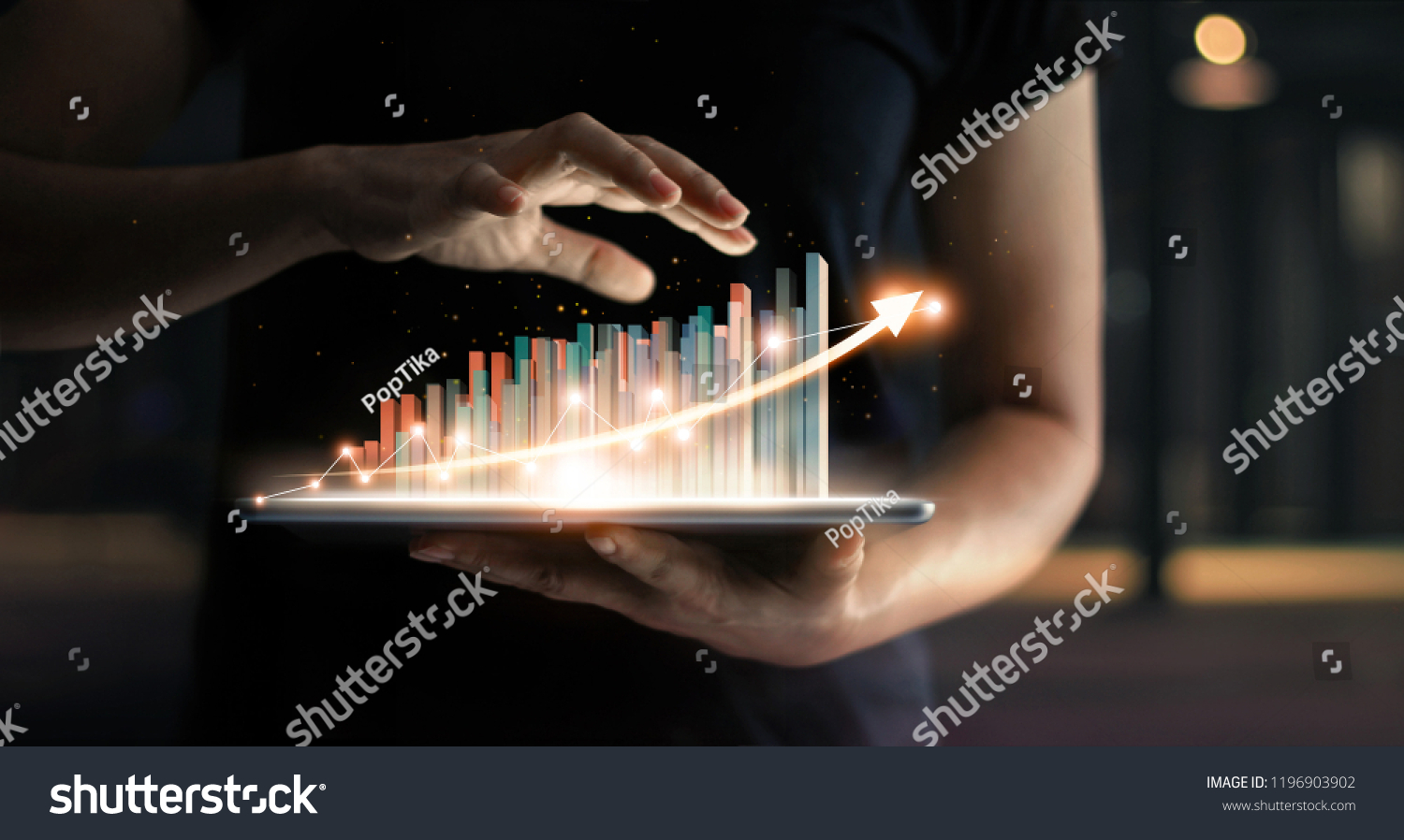 businessman holding tablet and showing a growing virtual hologram of statistics, graph and chart with arrow up on dark background. Stock market. Business growth, planing and strategy concept.  #1196903902