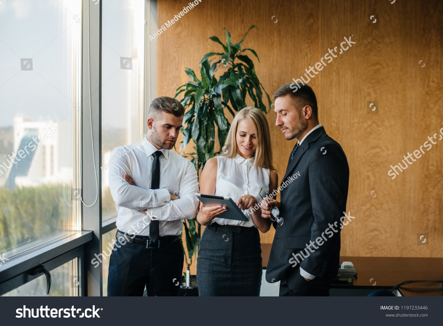 The employees of the firm are discussing the contract standing near the window. Business. Office. Finance. #1197233446