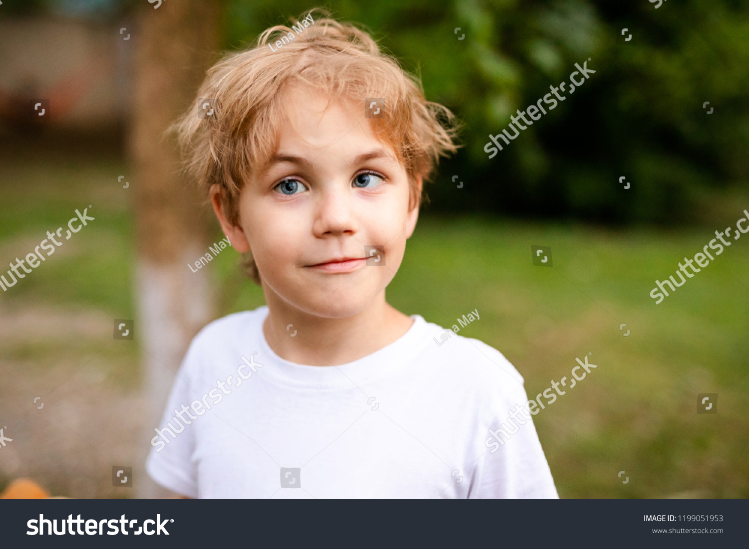 Blonde smiling boy with strabismus in warm park #1199051953