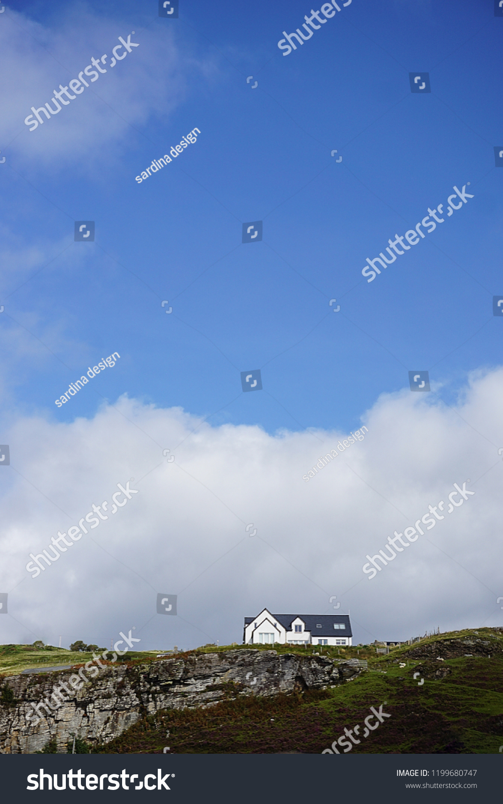 ELGON, SCOTLAND. AUGUST, 2018: White house with black tiled roof surrounded by clouds in the top of a green hill in Scotland in the island of Skye.                    #1199680747