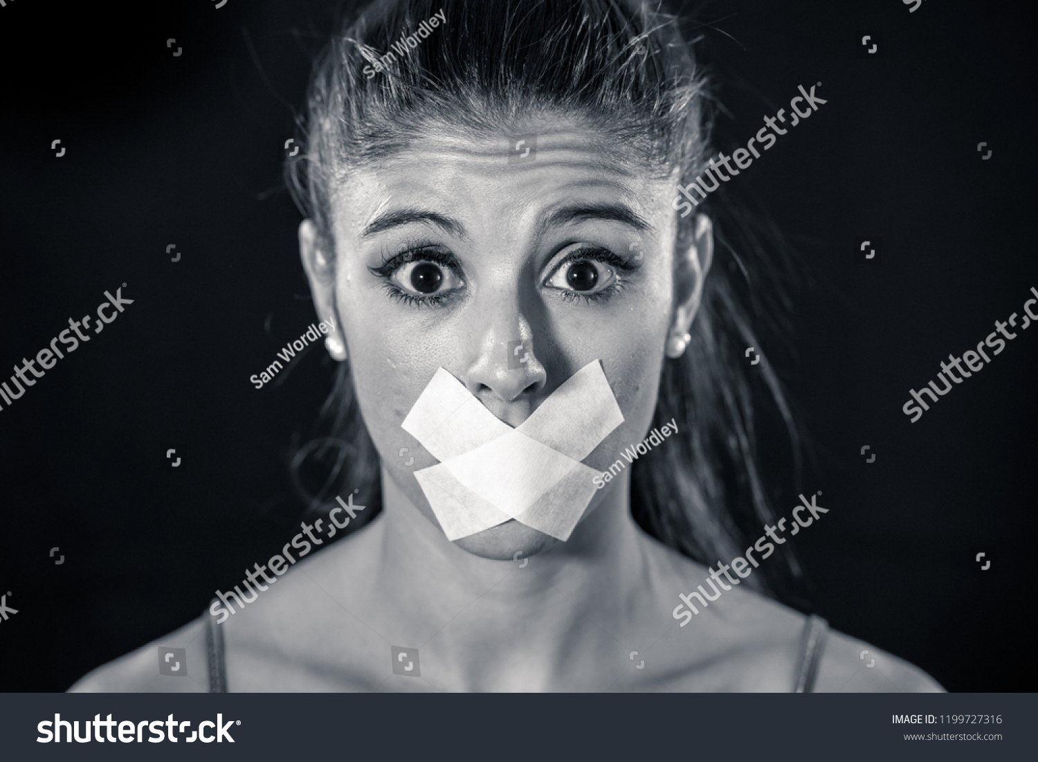 Attractive scared woman with taped mouth making in Silence Abuse Censorship Me too and Freedom of speech Concept Isolated on black background. #1199727316