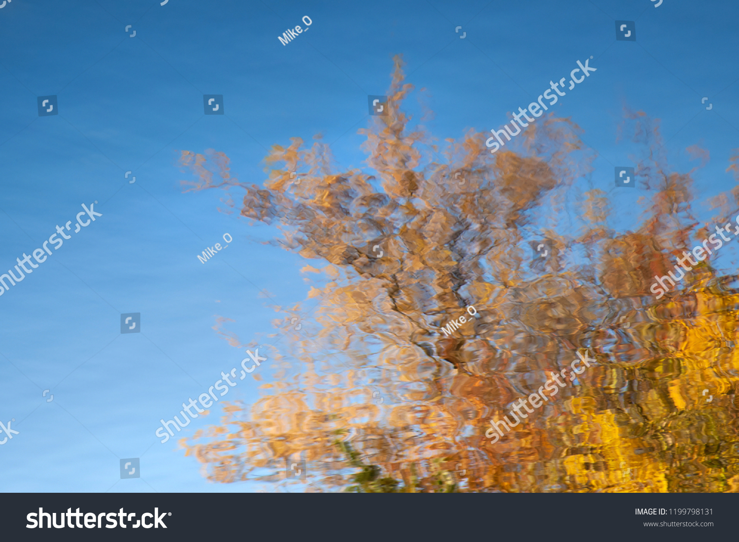 Abstract background: reflection of the autumn deciduous tree in the pond. Blue sky and yellow leaves reflecting in a lake. Water ripples #1199798131