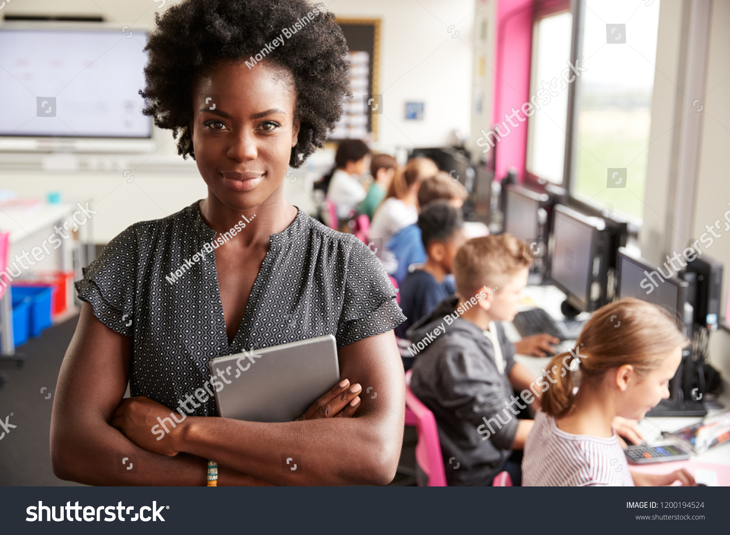 Portrait Of Female Teacher Holding Digital Tablet Teaching Line Of High School Students Sitting By Screens In Computer Class #1200194524