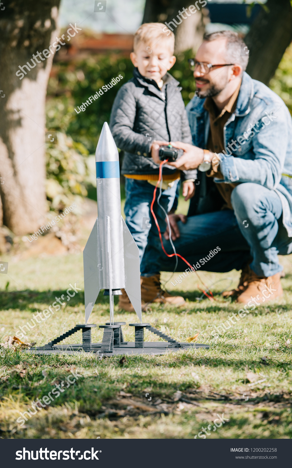 close-up view of model rocket and father with son playing behind #1200202258