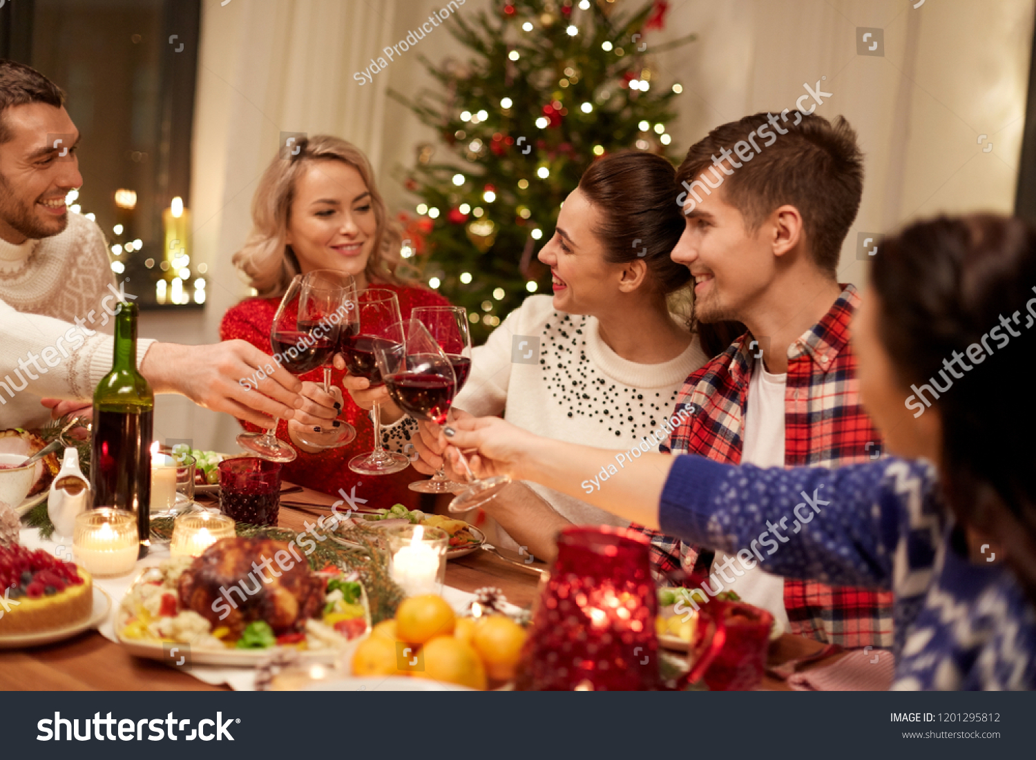 holidays and celebration concept - happy friends having christmas dinner at home, drinking red wine and clinking glasses #1201295812